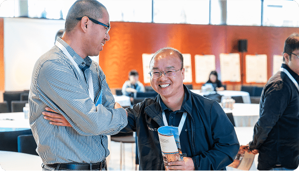 Two Structure Therapeutics employees wearing glasses and event lanyards chat warmly at an indoor biopharma conference.